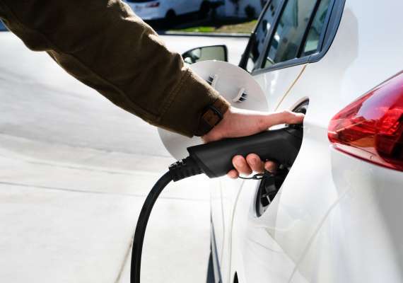 Person plugging charging cable into white EV parked in driveway